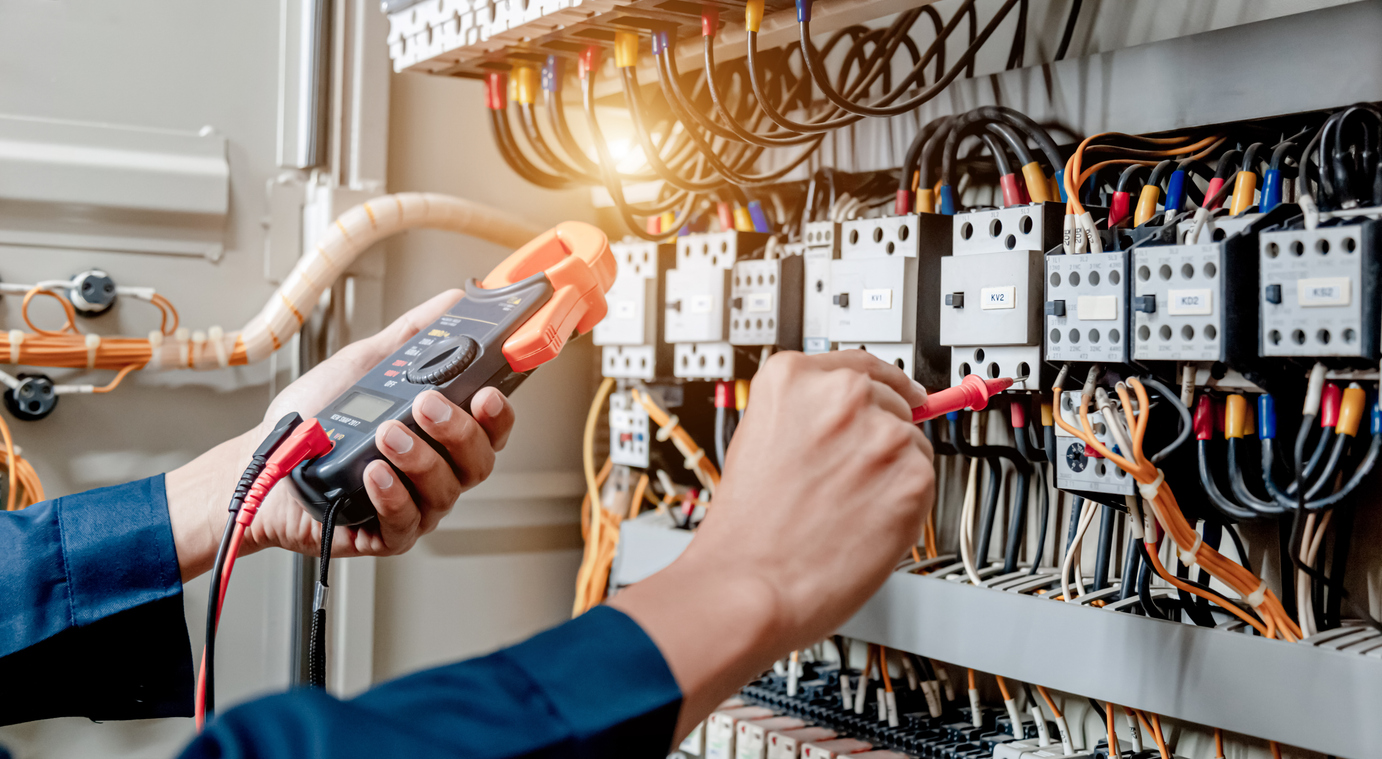 Electrician engineer uses a multimeter to test the electrical installation and power line current in an electrical system control cabinet. Electrical testing and tagging services